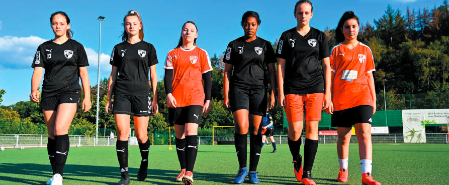 Sechs Fußballerinnen, in einer Reihe auf dem Rasen, in einer Vorwärtsbewegung