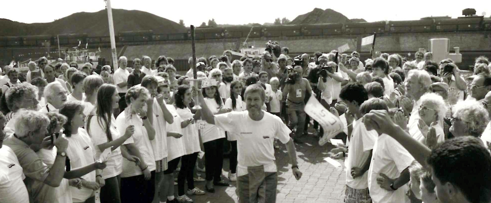 Schwarz-weiß Foto mit einem Mann, der mit einer Fackel zur Eröffnung einläuft, beidseitig am Wegesrand stehen viele Zuschauer.