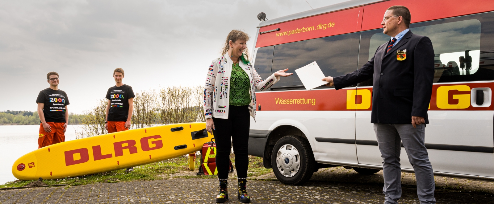 Eine Frau überreicht vor einem Rettungswagen eine Urkunde an einen Mann des DLRG