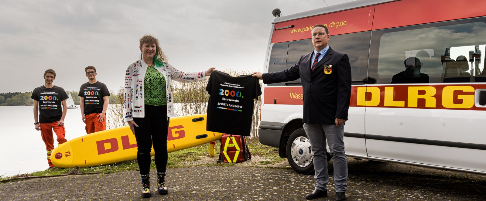 Ein Mann und eine Frau halten ein Tshirt hoch, im Hintergrund stehen zwei weitere Männer neben einem Rettungswagen