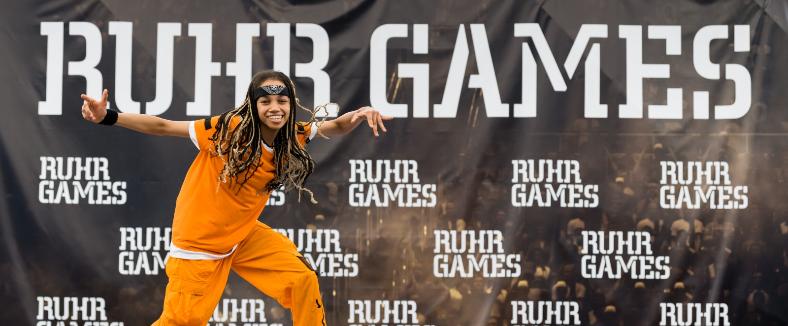 Junger Mann tanzt vor einer Plakatwand mit der Aufschrift Ruhr Games