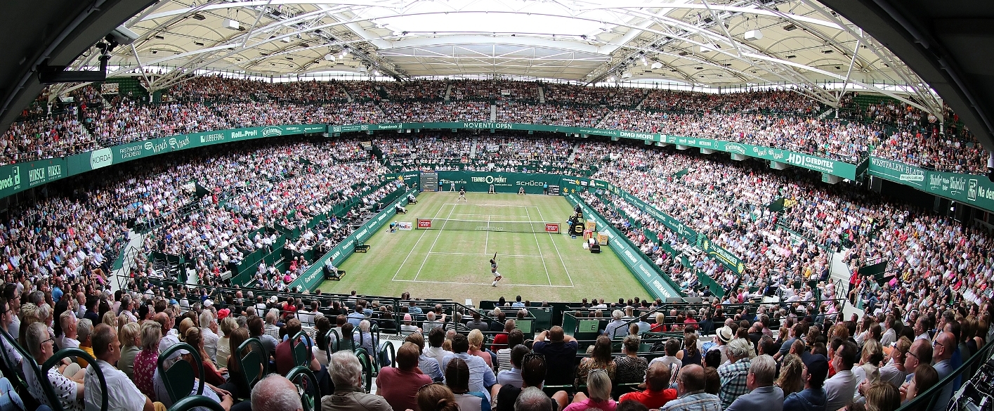 Tennis Arena in Fischaugenperspektive. Auf dem Feld spielen zwei Tennisspieler, während das ausverkaufte Stadion gespannt zuschaut.