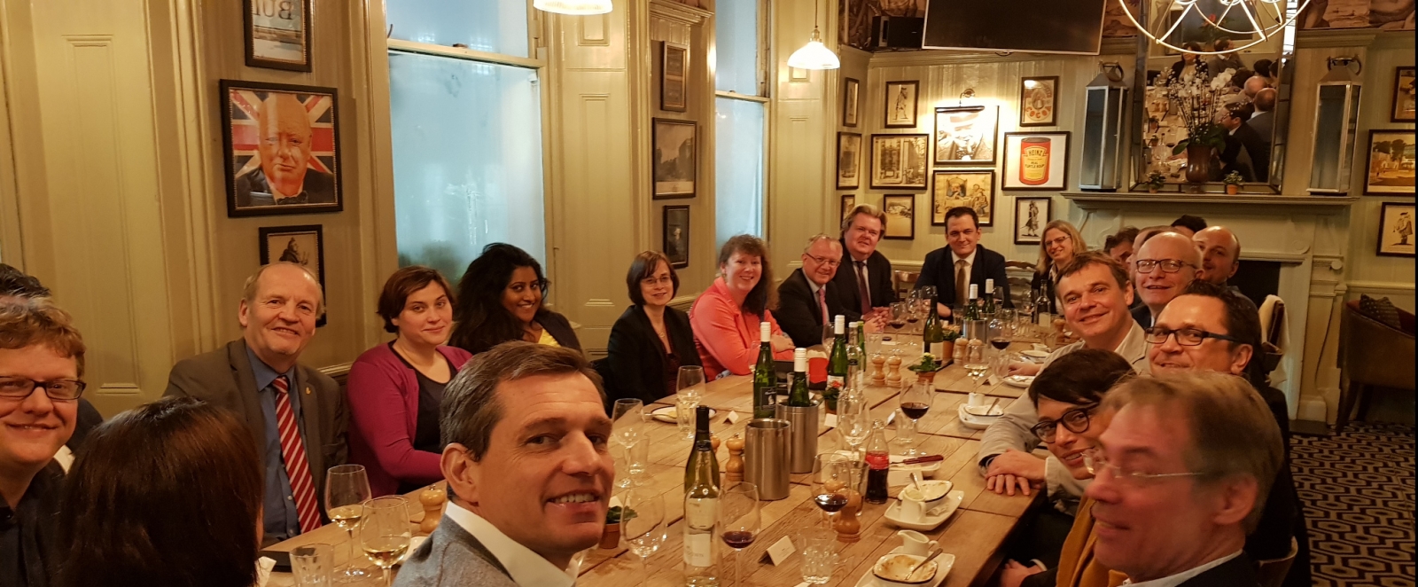 Staatssekretärin Milz sitzt mit dem Sportausschuss in London beim Essen an einem großen Tisch zusammen. An Wänden hängen überall eingerahmte Bilder.