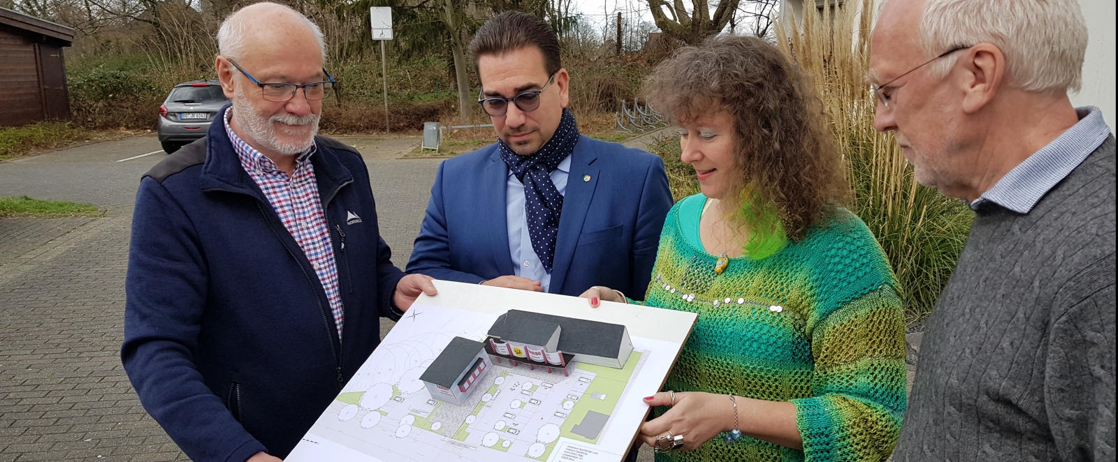 Staatssekretärin Milz (rechts) schaut sich mit drei Herren vom Badminton Club  einen Bauplan an. Sie stehen gemeinsam im Freien.