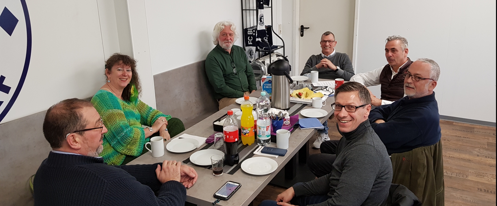 Staatssekretärin Milz sitzt mit Mitgliedern des FC Blau Weiss Friesdorf zusammen an einem gedeckten Tisch.