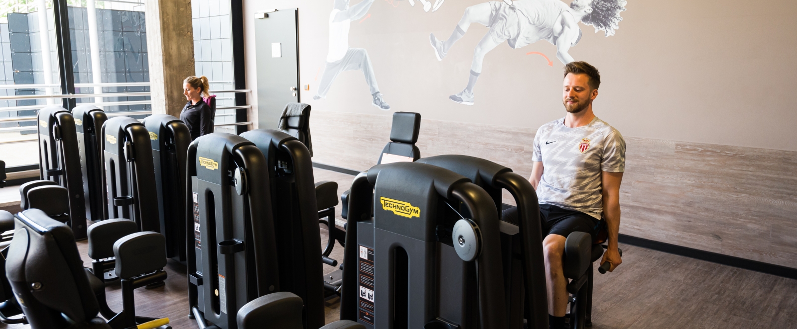 Zwei Trainierende sitzen auf fitnessgerten in einem Fitnessraum.