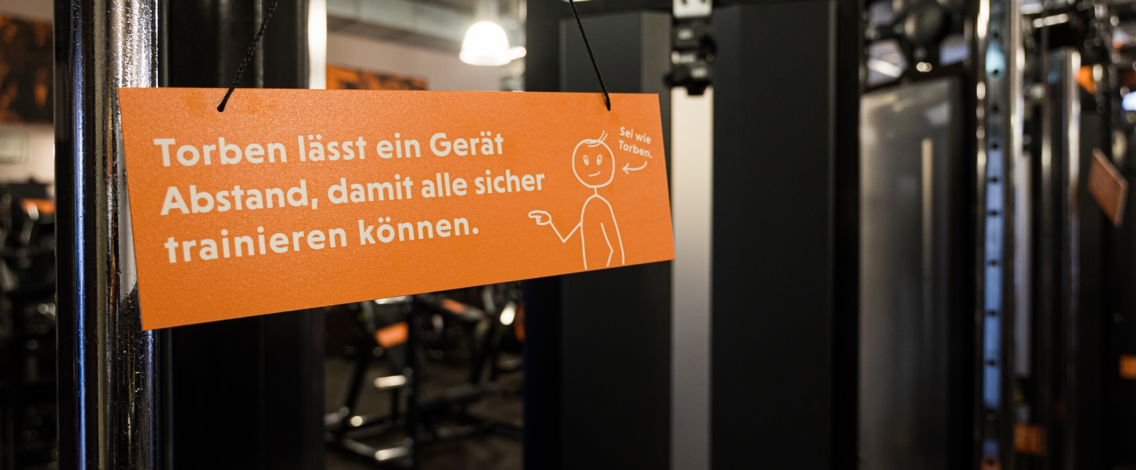 ein oranges Schild mit einem weißen Strichmännchen namens Torben und weißen Text dient alls Abstandshalter beim Training.