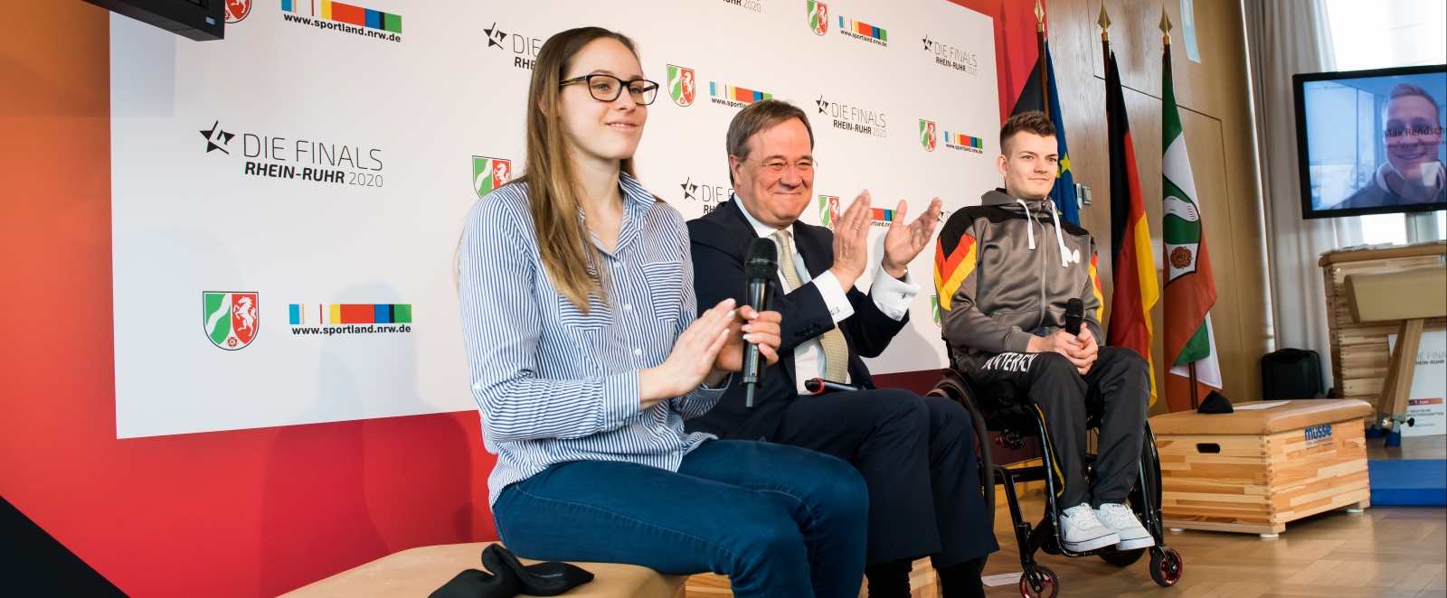 Ministerpräsident Laschet sitzt neben einer jungen Dame und einem jungen Tischtennisspieler im Rollstuhl, alle haben ein Mikrofon.