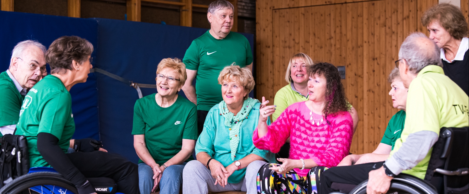 Staatssekretärin Milz sitzt mit mehreren Sportlern in einer Sporthalle. Links sitzt eine Dame im Rollstuhl, rechts ein Herr im Rollstuhl.