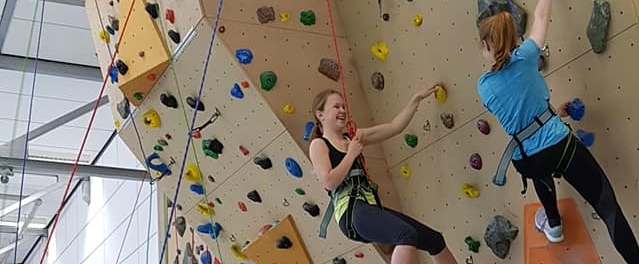 Jugendliche kletten eine Indoor-Kletterwand hinauf.