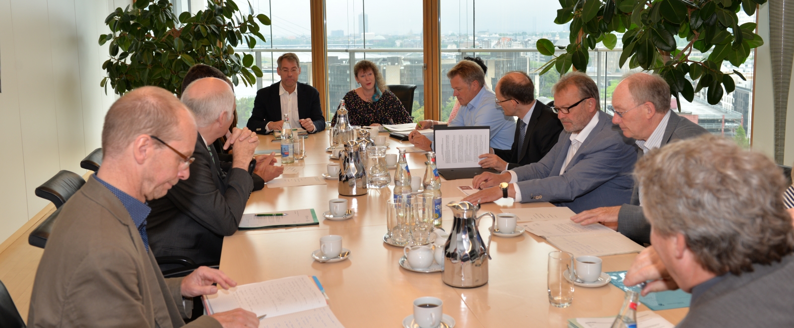 Staatssekretärin Milz sitzt mit den Mitgliedern des Arbeitstreffen an einem langen Tisch. Im Hintergrund sieht man den Ausblick über eine Stadt.