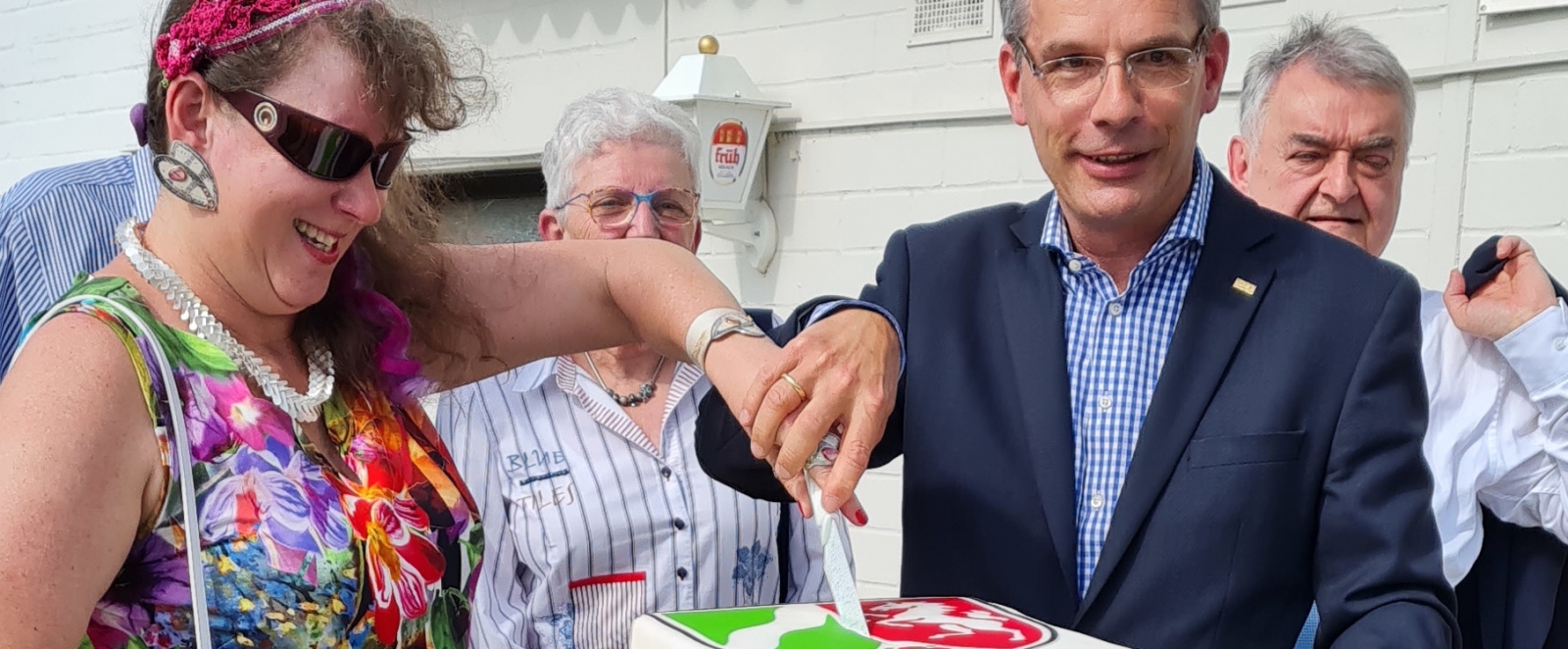 Staatssekretärin Milz schneidet mit einem Herrn den Sportland-NRW-Kuchen an.