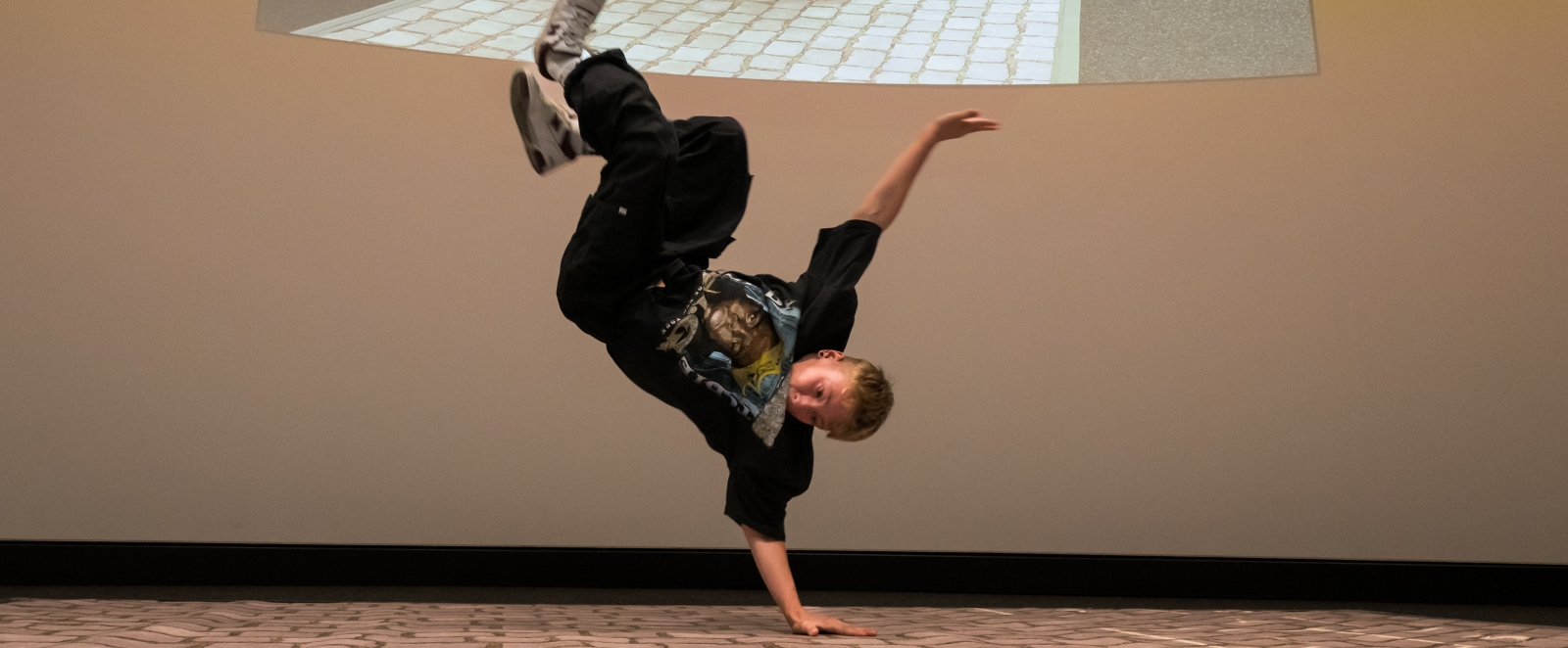 Ein Breakdancer bei seiner Showeinlage, er liegt kopfüber in der Luft, während er sich mit einer Hand vom Boden abstützt.