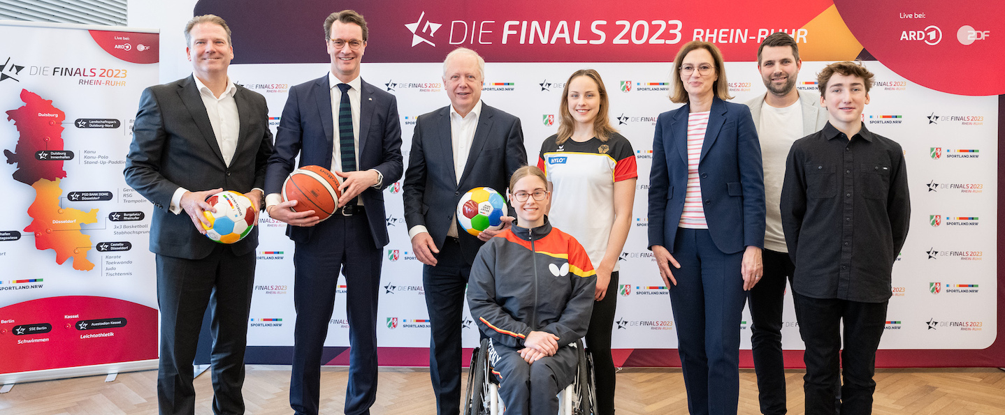 Mehrere Personen vor Sponsorenwand zu den Finals 2023