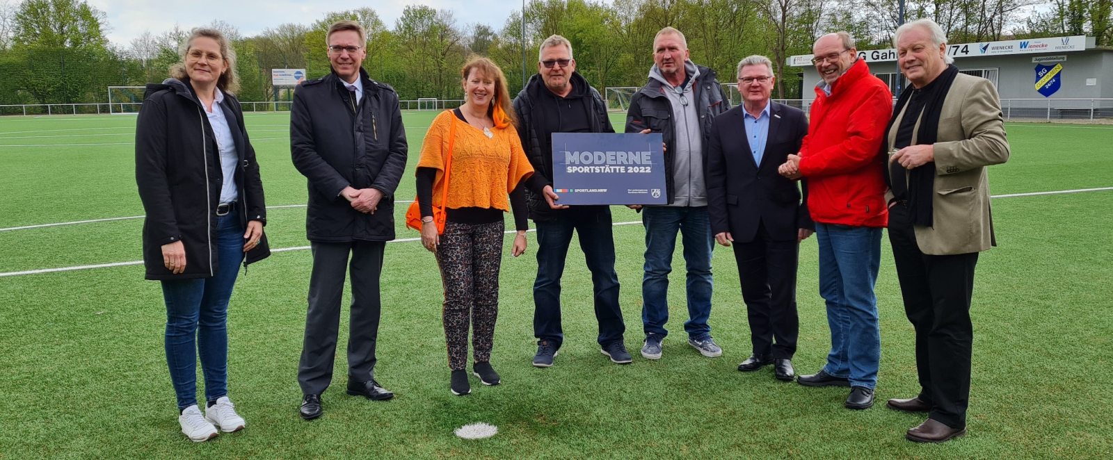 Personen auf Fußballplatz mit Schild Moderne Sportstätte 2022