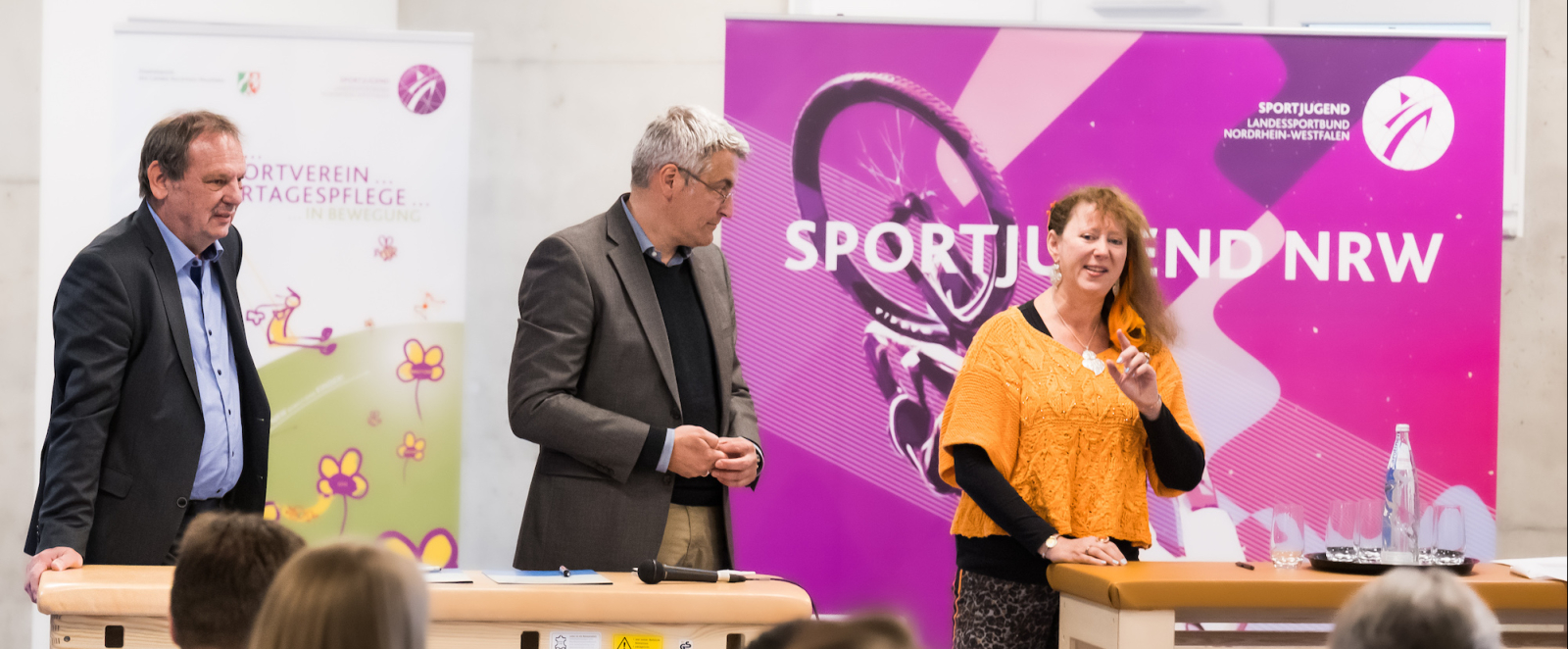 Mehrere Personen mit Andrea Milz vor rosafarbenem Banner