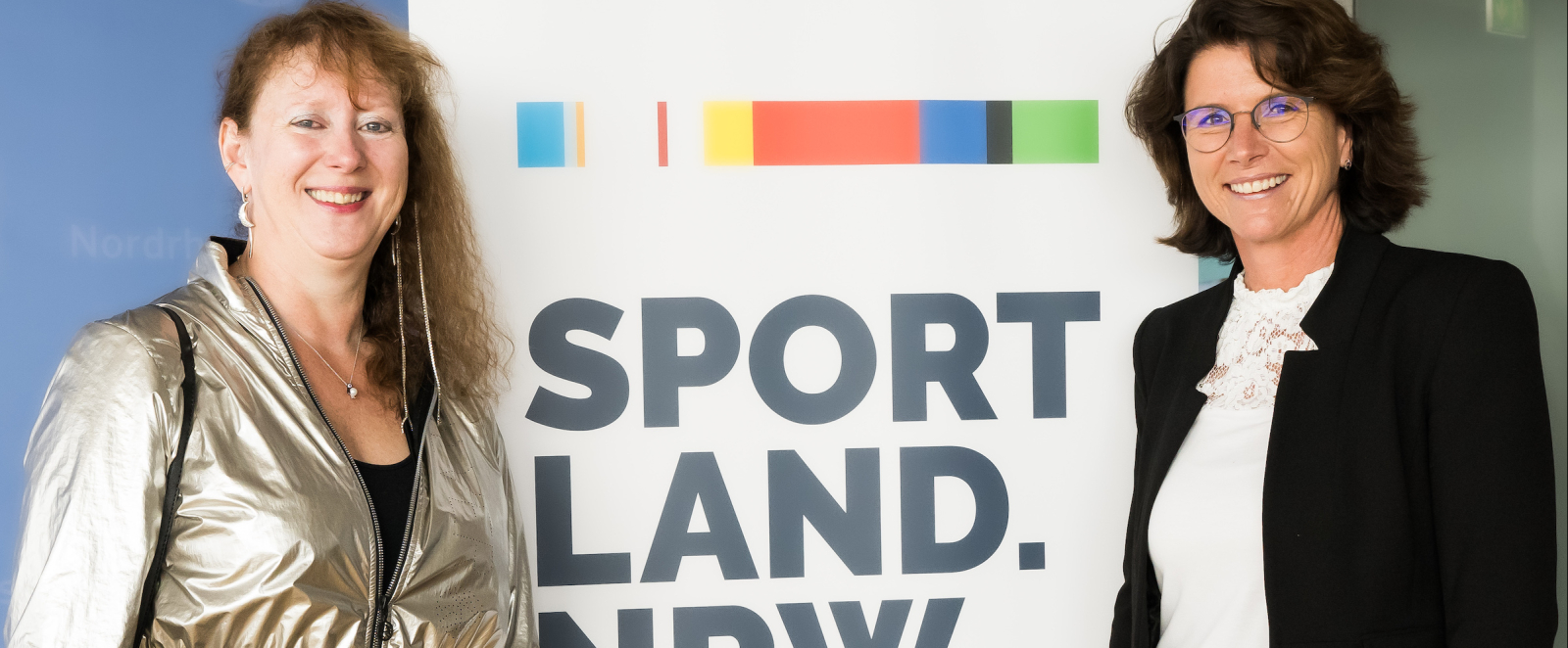 Andrea Milz und eine Frau vor Banner des Sportland.NRW