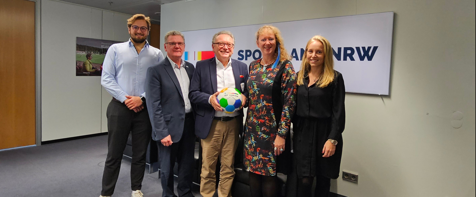 Fünf Personen in einem Flur vor Sportland.NRW Banner 