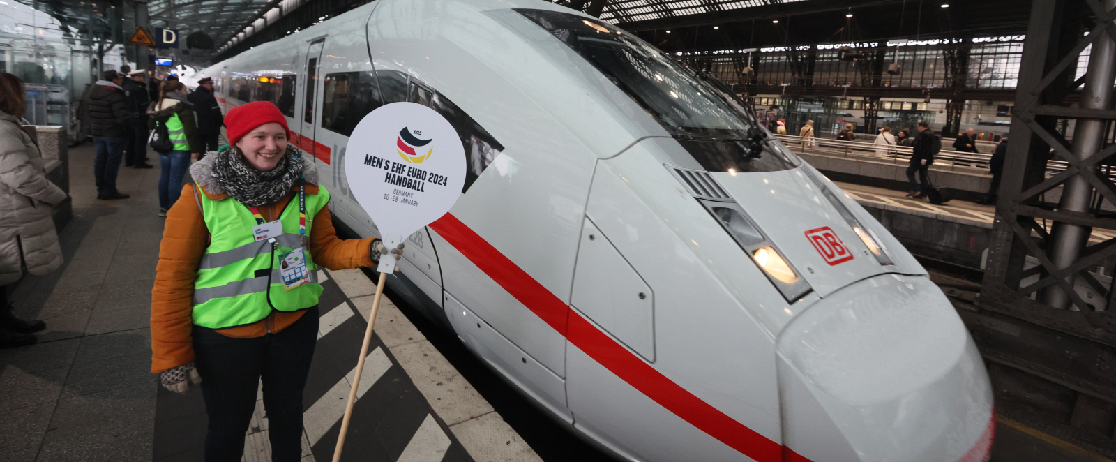 Frau hält Handball-EM-Schild vor ICE am Bahnhof Köln