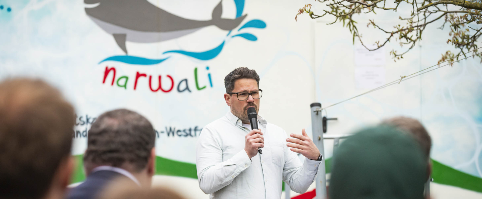 Mann mit Mikrofon vor dem narwali Schwimmcontainer