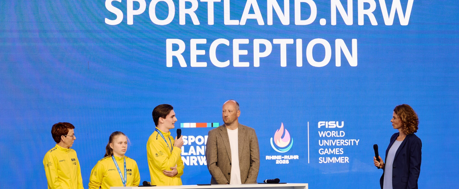 Fünf Personen auf einer Bühne mit blauem Hintergrund bei der Sportland.NRW Reception