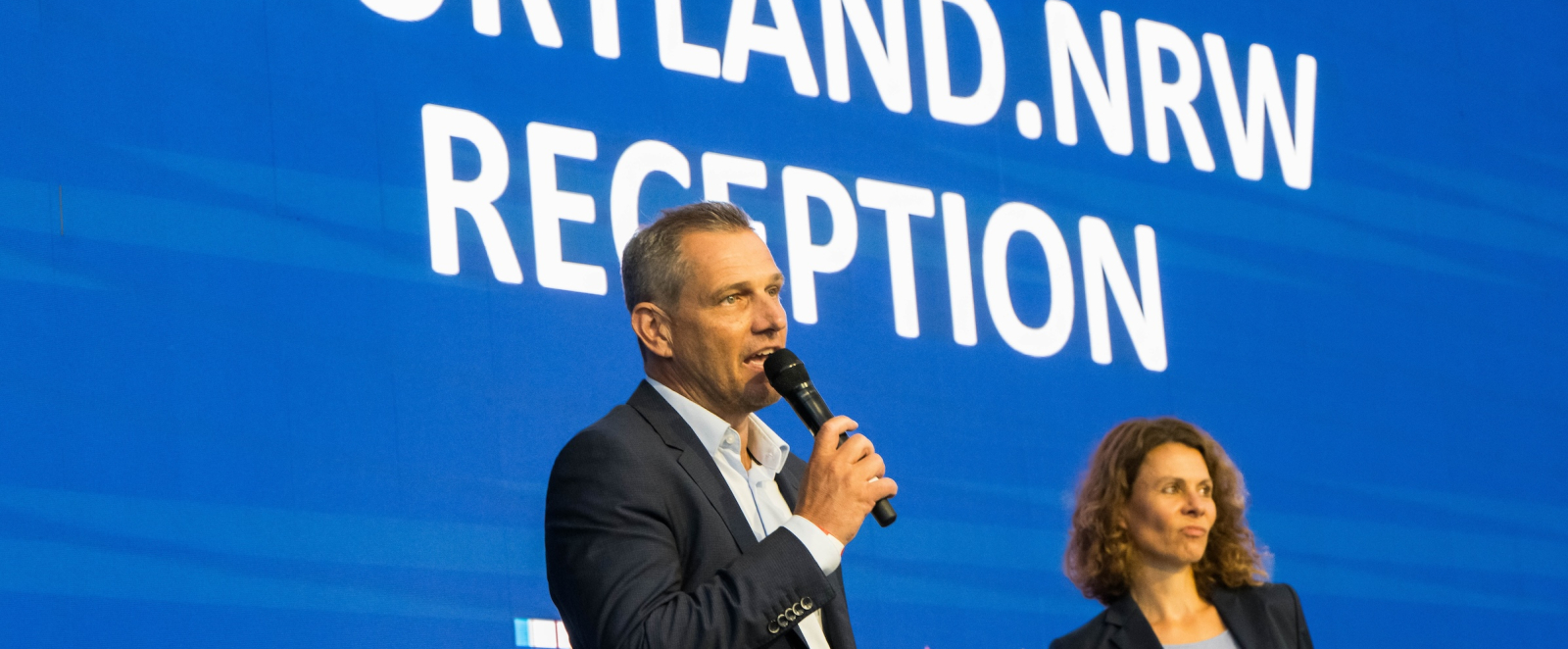 Zwei Personen vor blauem Hintergrund und Schriftzug Sportland.NRW-Reception