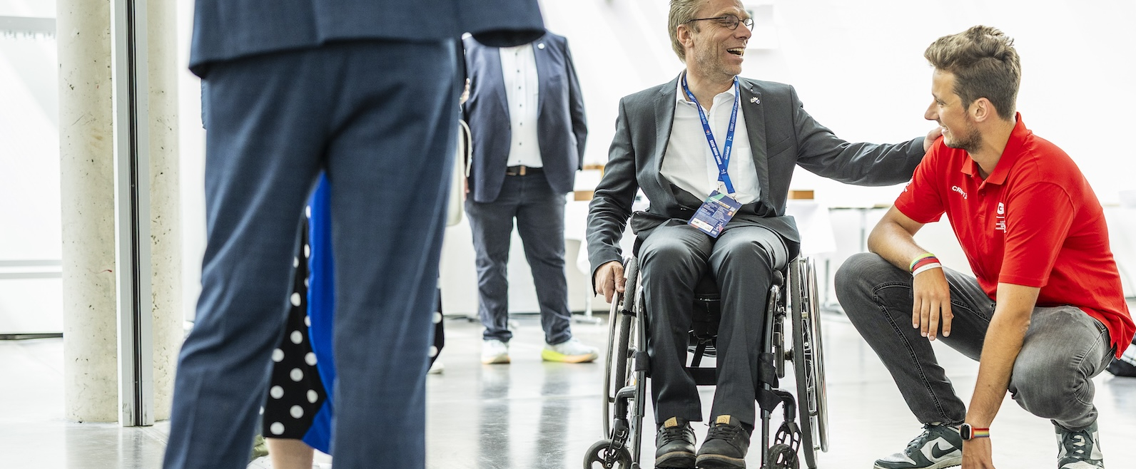 Rollstuhlfahrer mit knieender Person in rotem Hemd