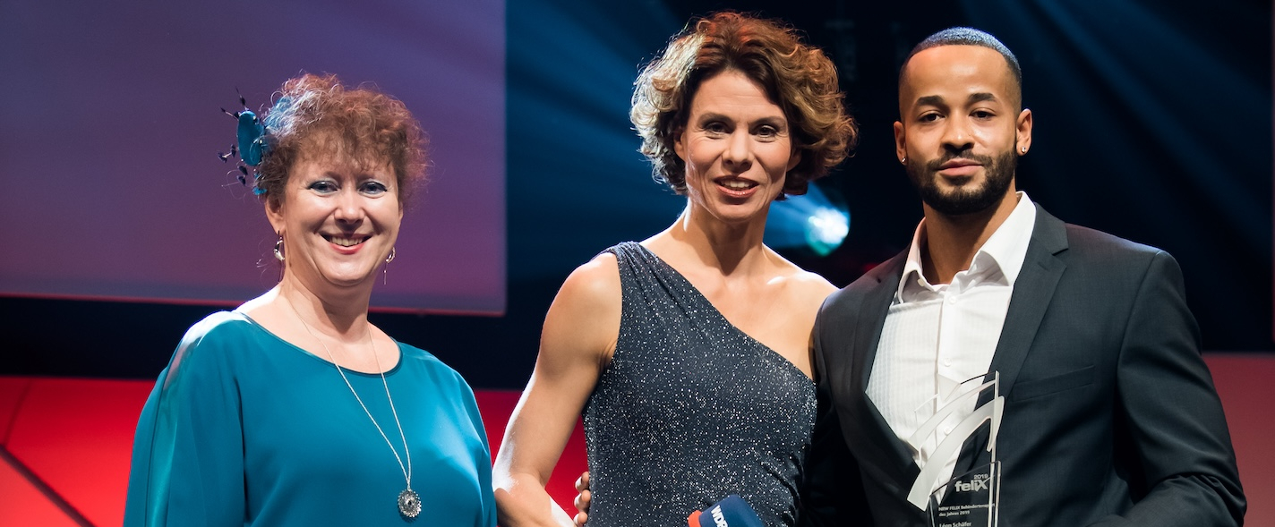 Links steht Staatssekretärin Andrea Milz im dunkelgrünen Kleid, in der Mittte die Moderatorin und rechts von ihr steht Leon Schäfer mit einem Felix-Award in seiner linken Hand.