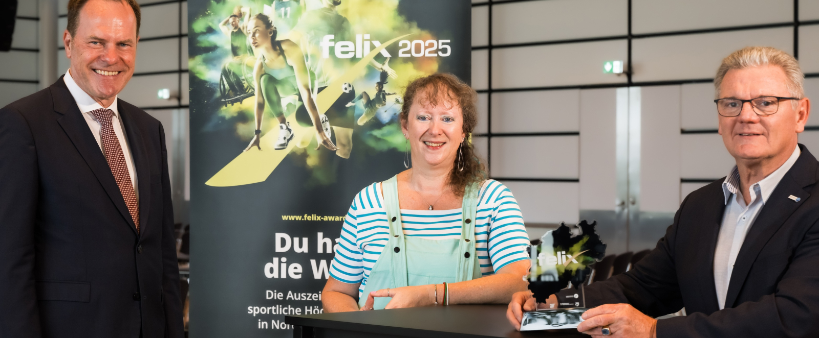 Andrea Milz mit zwei Personen vor dem Plakat zum felix award