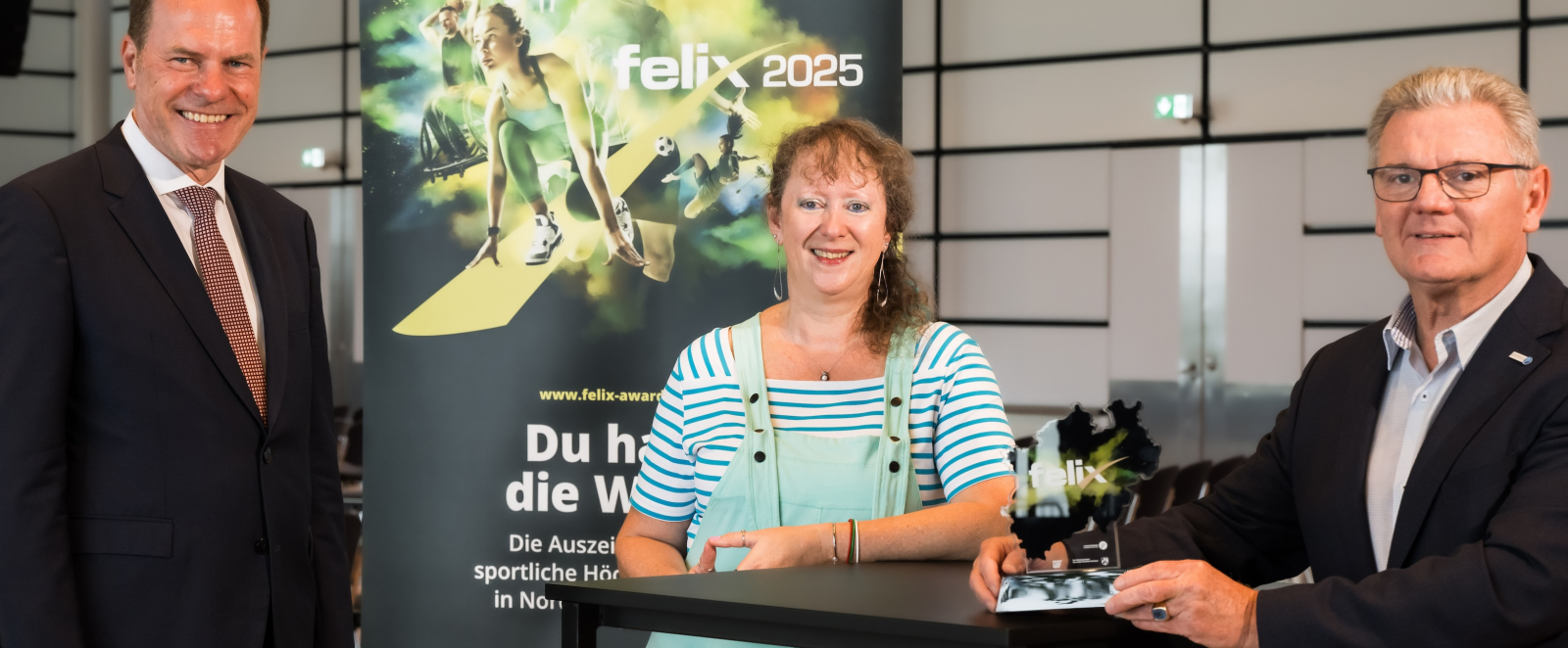 Andrea Milz mit zwei Personen vor dem Plakat zum felix award
