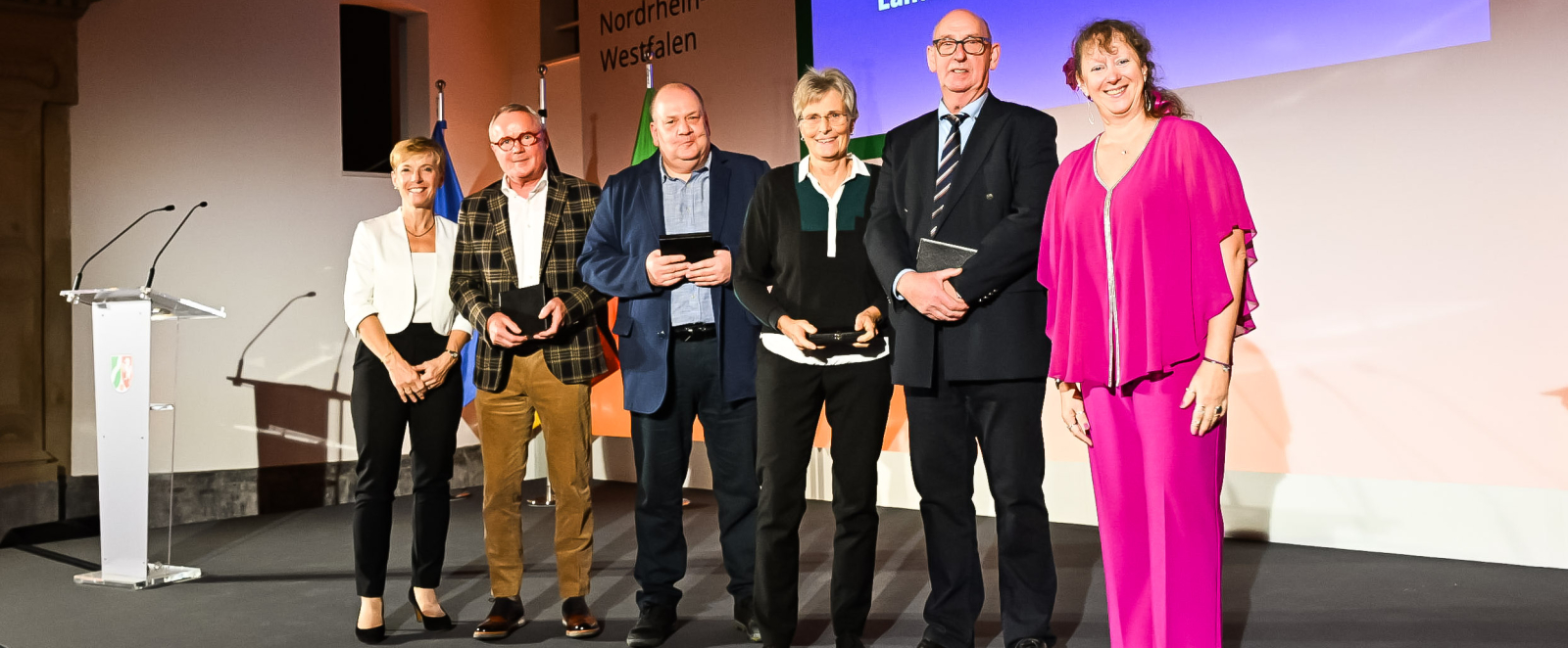 Geehrte bei der Verleihung der Sportplakette auf einer Bühne mit Andrea Milz