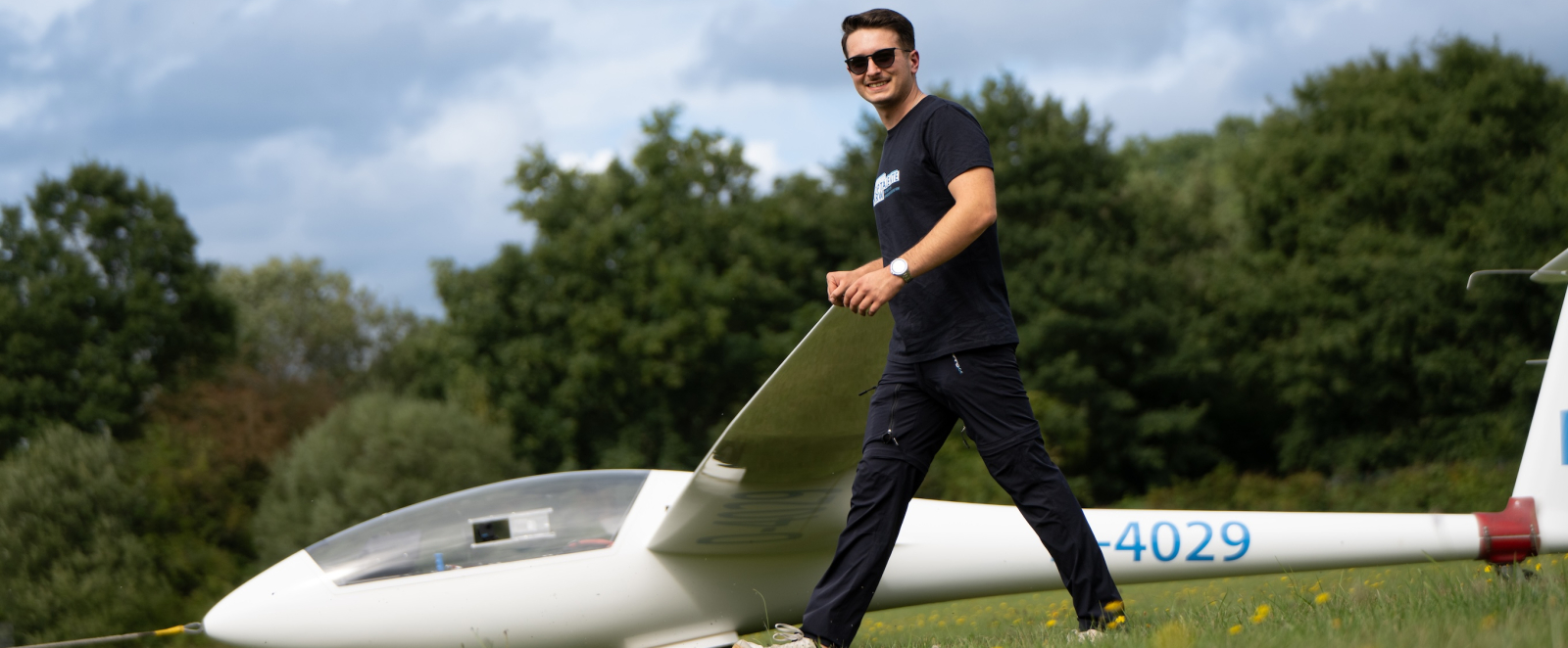 Person in dunkler Kleidung hinter einem Flügel eines Segelflugzeugs am Boden