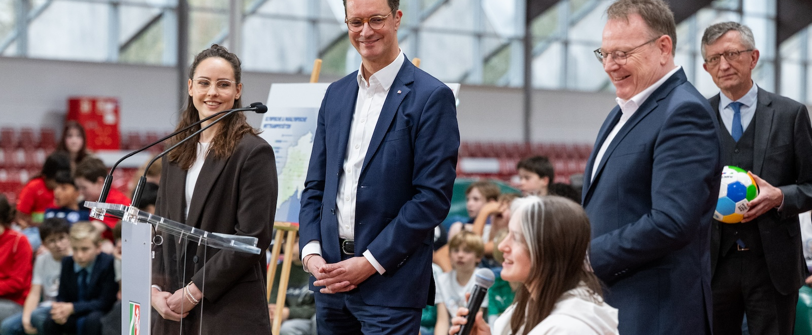 Rollstuhlfahrerin mit einem Mikrofon in der Hand neben Hendrik Wüst 