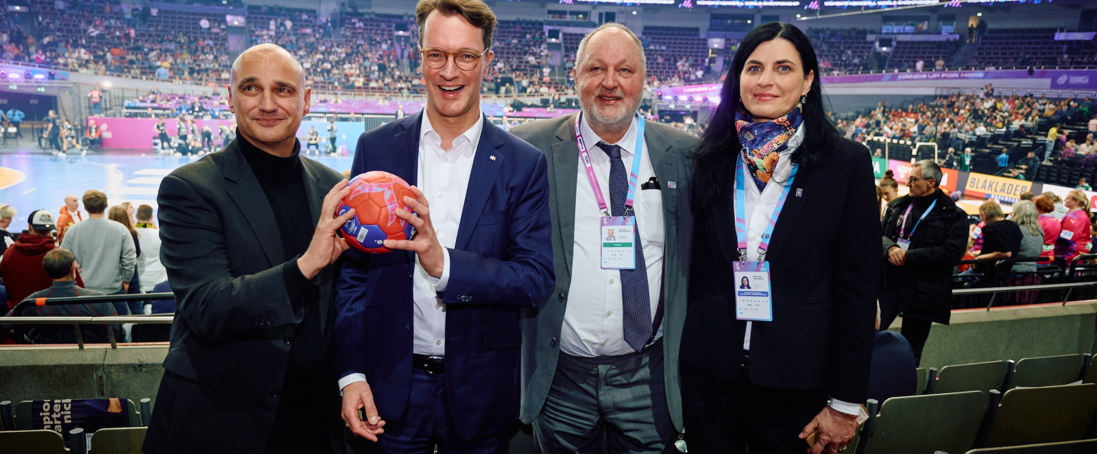 Hendrik Wüst und weitere drei Personen auf der Tribüne mit Blick auf das Spielfeld