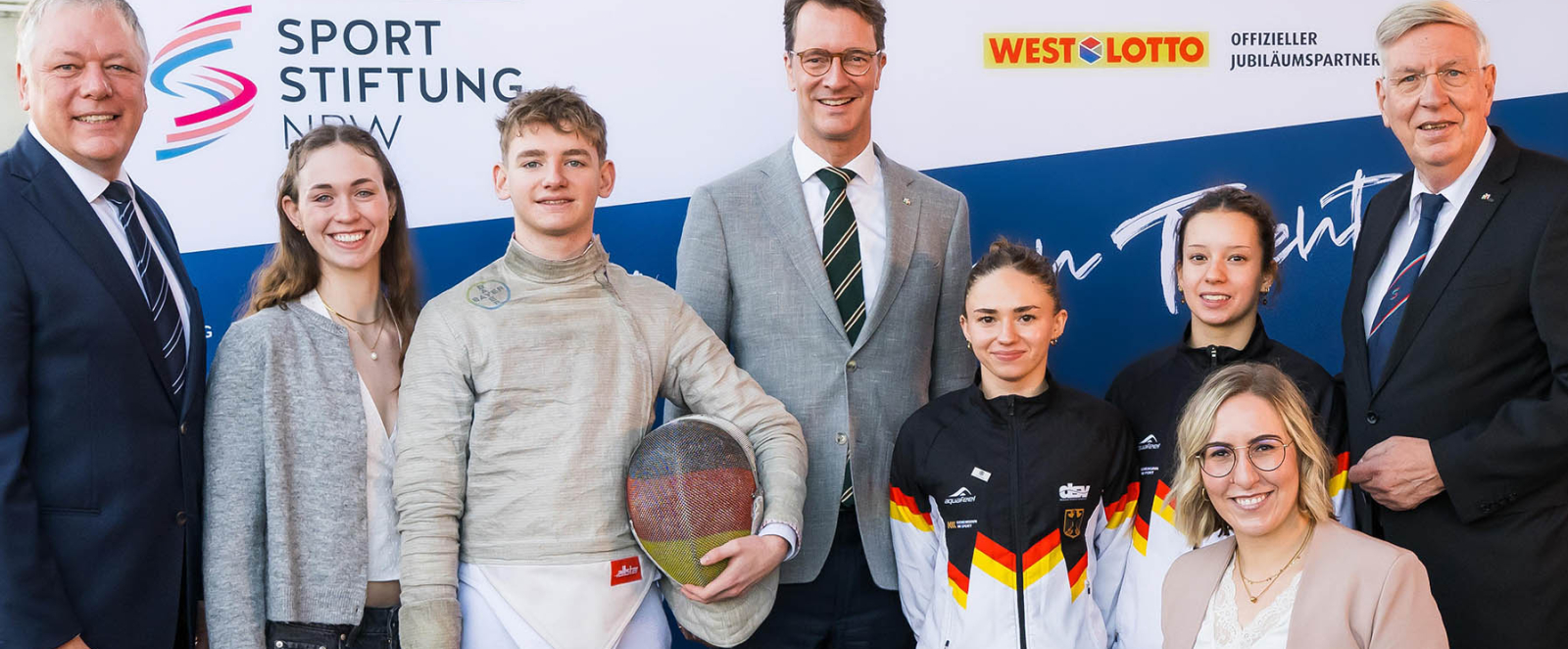 Acht Personen vor einem Sportstiftung NRW-Banner, in der Mitte Ministerpräsident Wüst