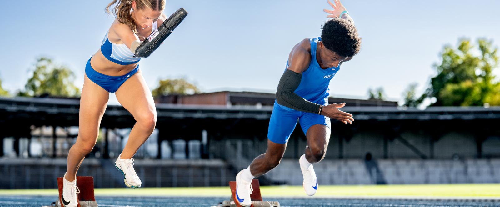 Zwei Athleten, eine mit Armprothese, kommen aus dem Startblock