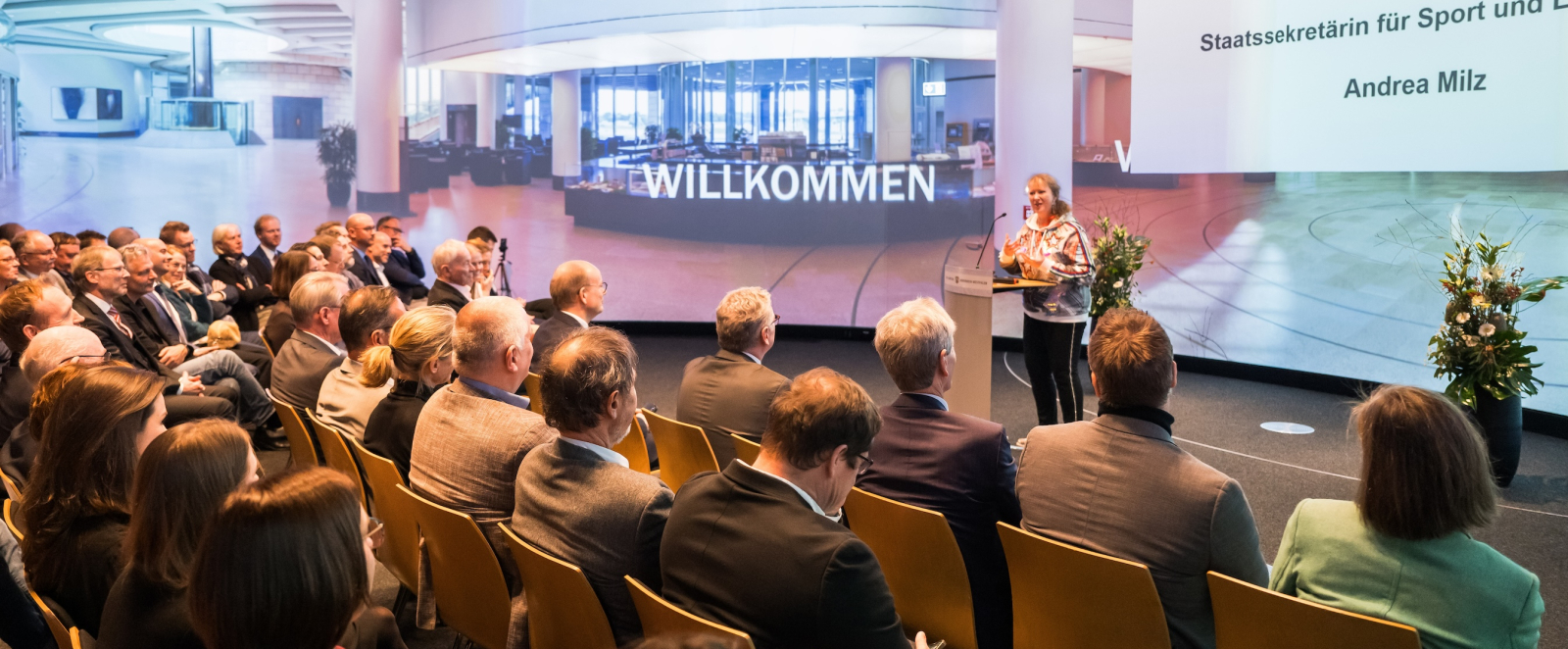 Blick auf die Bühne mit Andrea Milz, davor Stuhlreihen mit Personen
