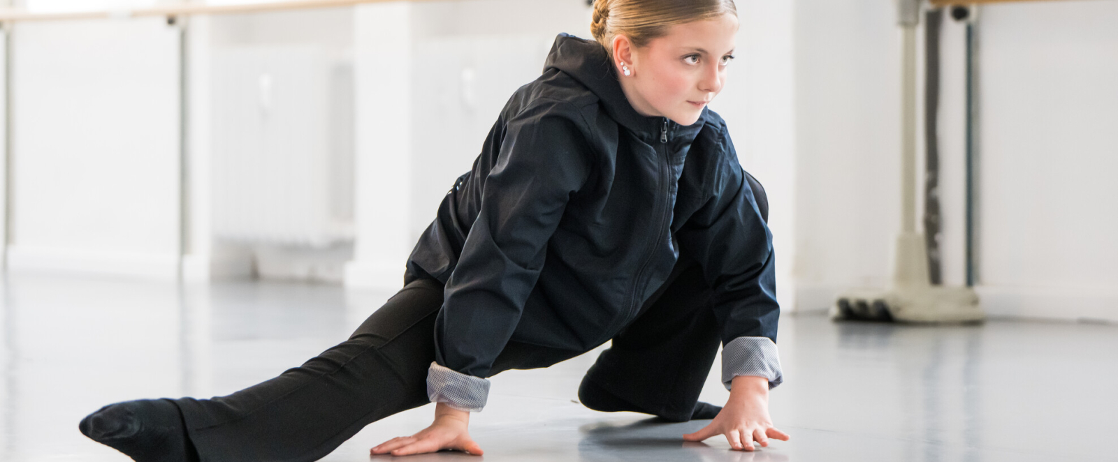 Junge Frau in dunkler Kleidung in Tanzpose mit Hände auf dem Boden in einem Studio