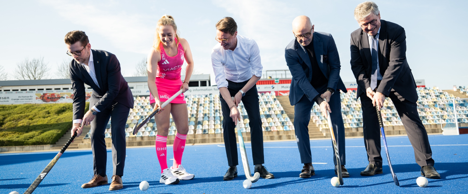 Wüst mit einer Hockeyspielerin in pinkem Dress sowie zwei weiteren Männern mit Hockeyschlägern