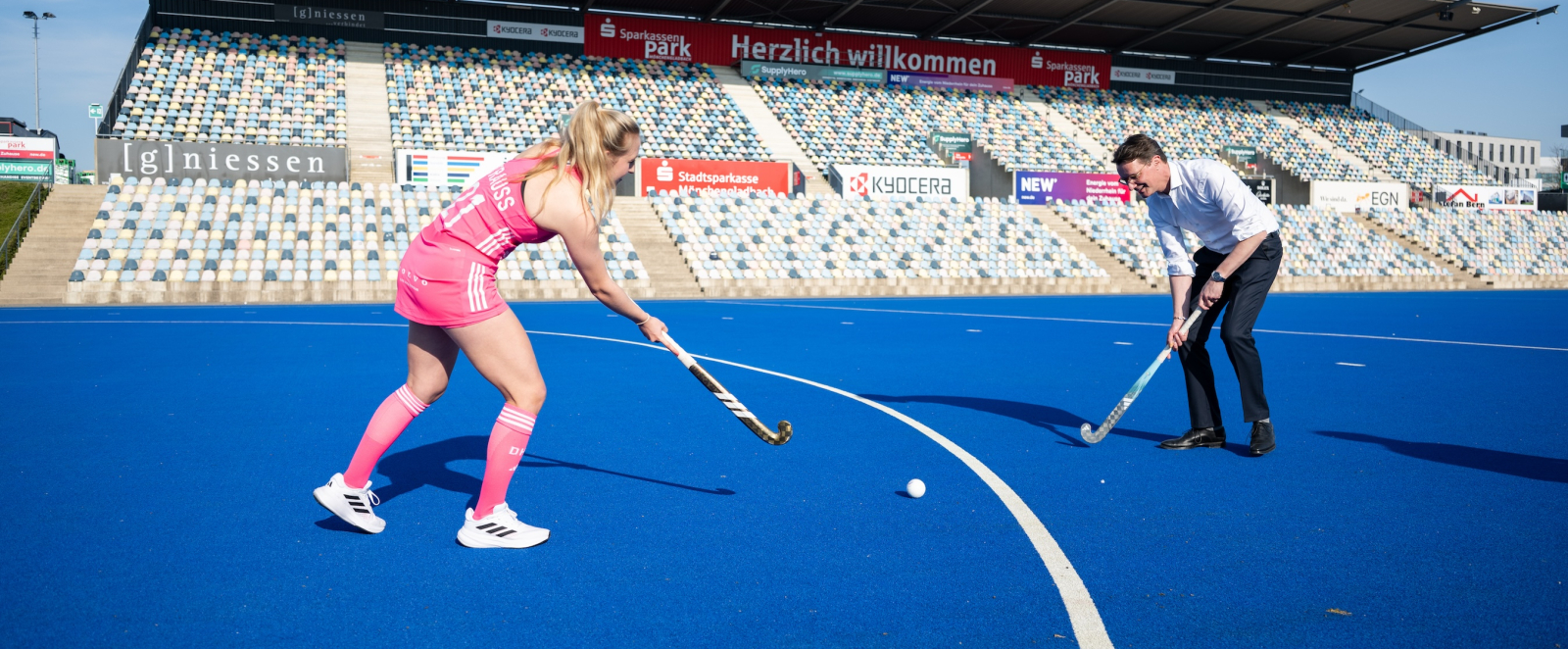 Ministerpräsident Wüst und eine Hockeyspielerin in pinkem Dress im Stadion mit blauem Untergrund