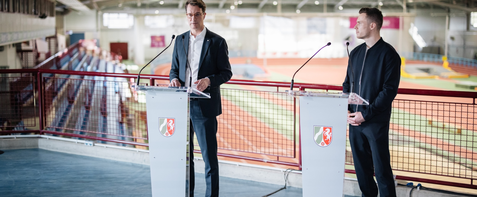 Hendrik Wüst und Markus Rehm an Rednerpulten mitten in der Leichathletik-Halle in Leverkusen