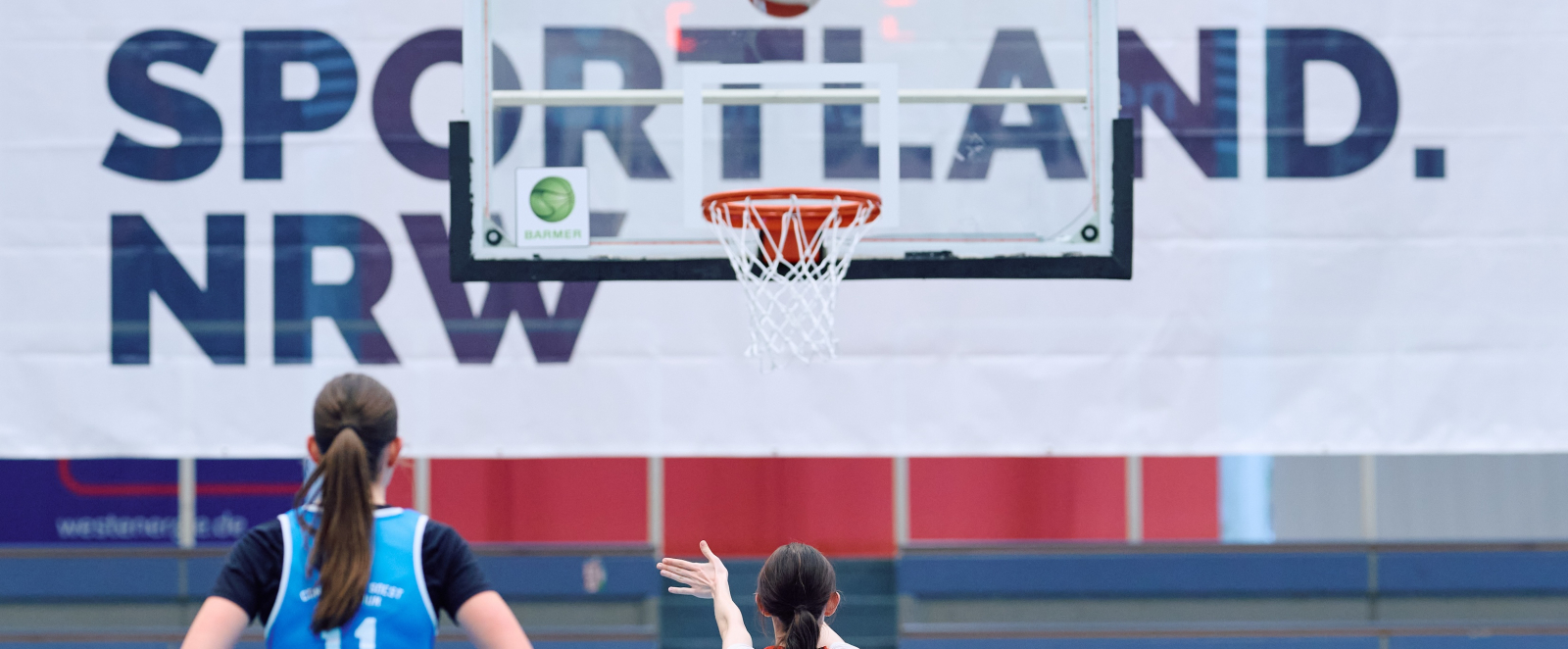Zwei Athletinnen beim Basketball vor einem Sportland.NRW-Banner
