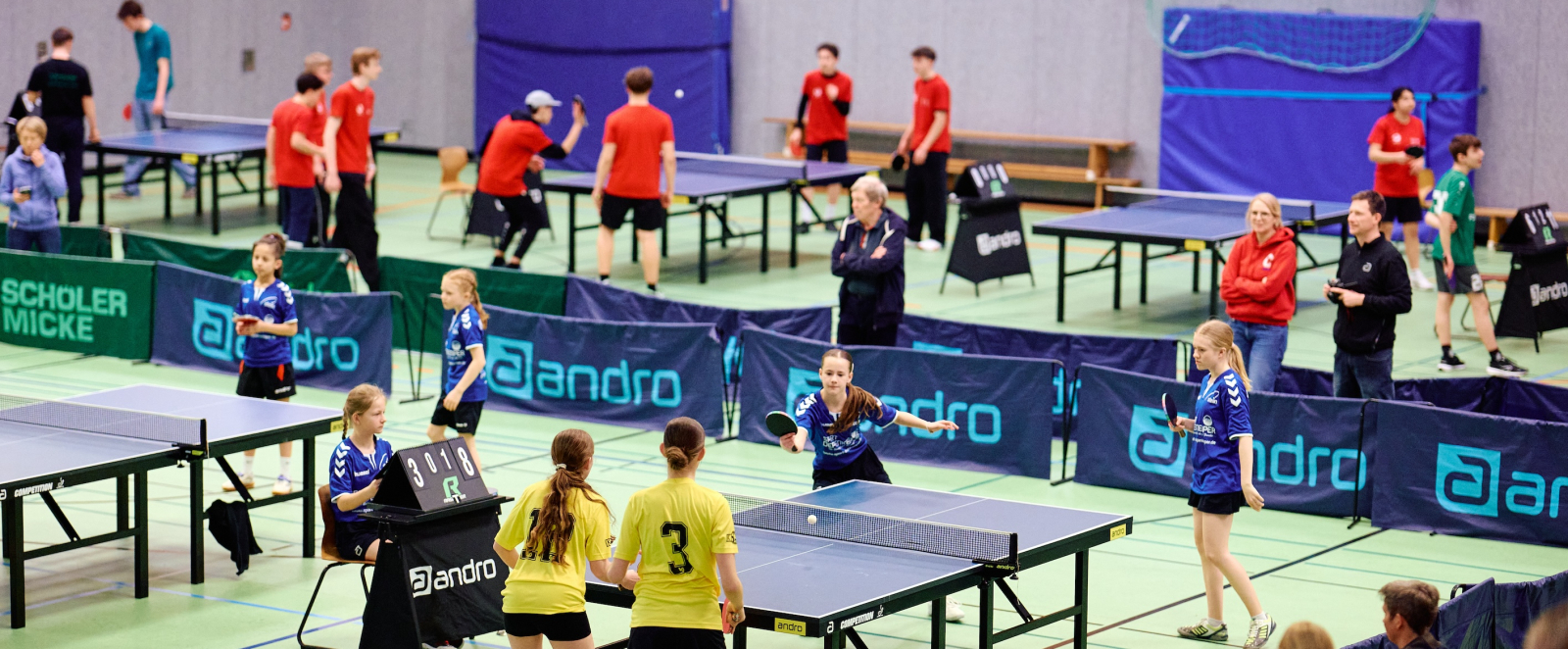Mehere Tischtennisplatten in einer Halle, an denen Schüler spielen