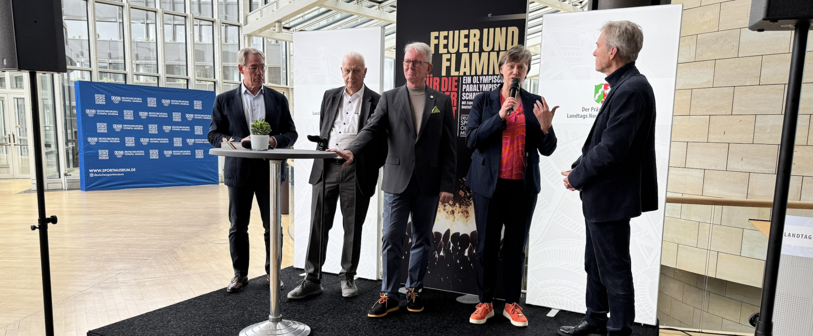 Mehrere Personen auf einem schwarzen Podium bei der Ausstellungseröffnung im Landtag NRW