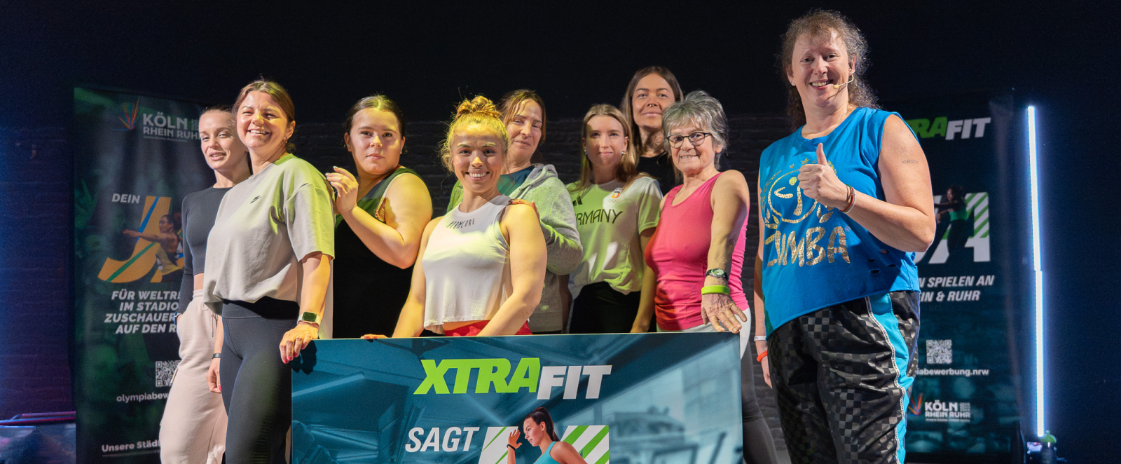 Andrea Milz und junge Frauen in einem Fitnessstudio halten ein KRR-Banner