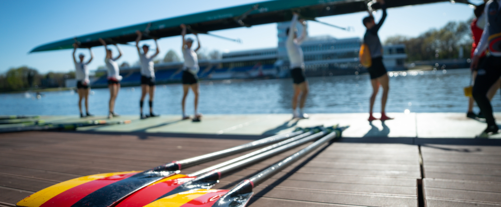 Ruderer mit dem Boot über dem Kopf, im Vordergrund Ruderblätter in den Deutschland-Farben