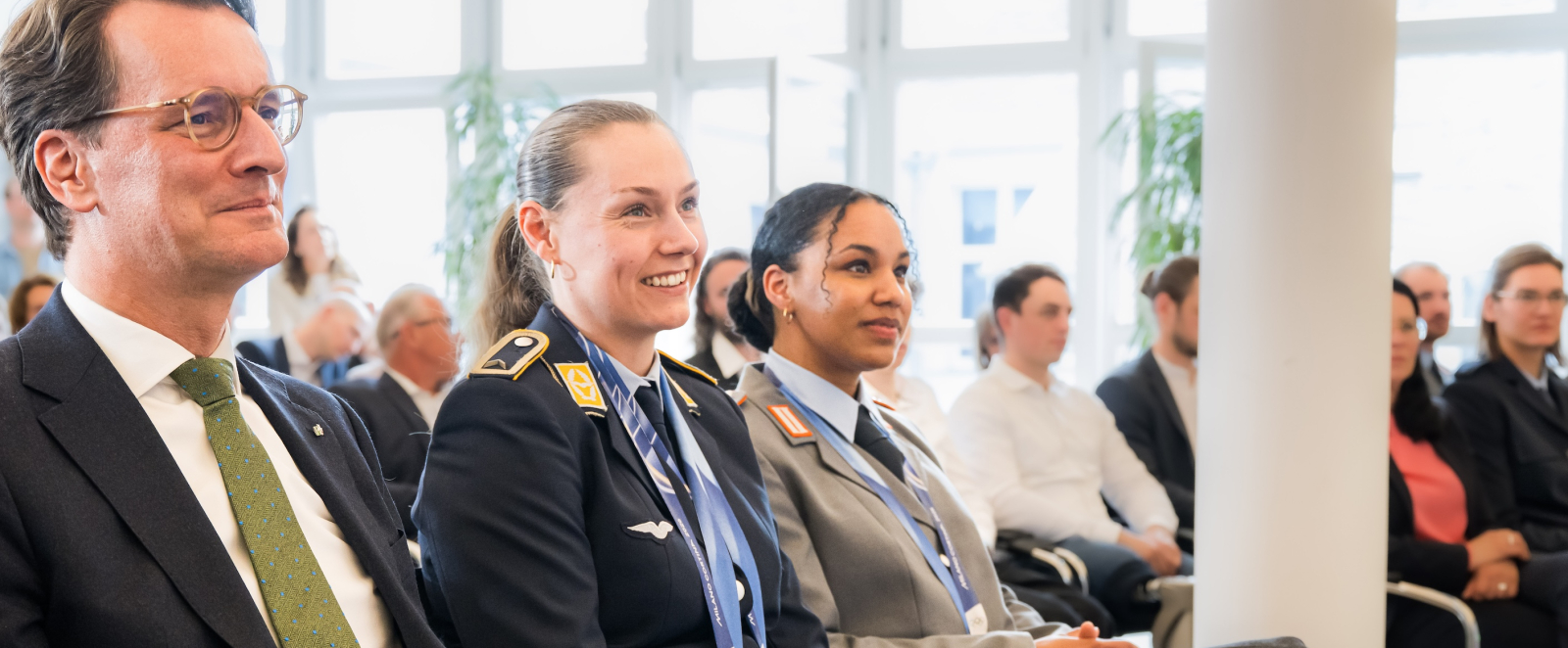 Hendrik Wüst sitzt neben Laura Nolte und Deborah Levi, im Hintergrund sind Fenster zu sehen