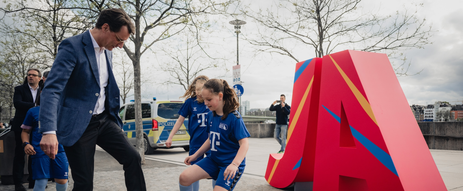 Ministerpräsident Wüst kickt einen Ball mit zwei jungen Mädchen vor den roten Buchstaben "JA"