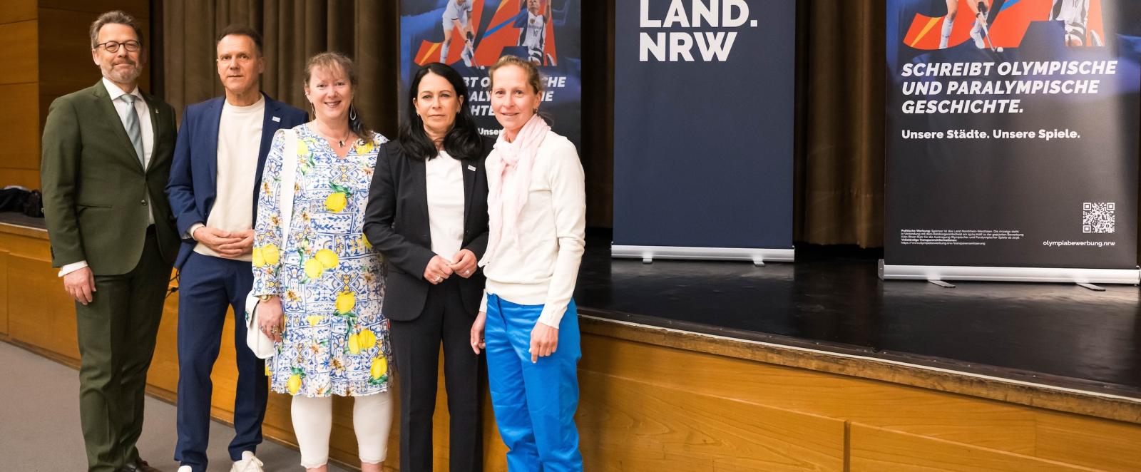 Andrea Milz sowie vier weitere Personen vor einer Bühne mit Aufstellern zur Bewerbung KölnRheinRuhr