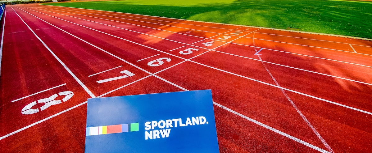 Blaues Schild mit Aufschrift "Sportland.NRW" liegt auf einer roten Tartanbahn